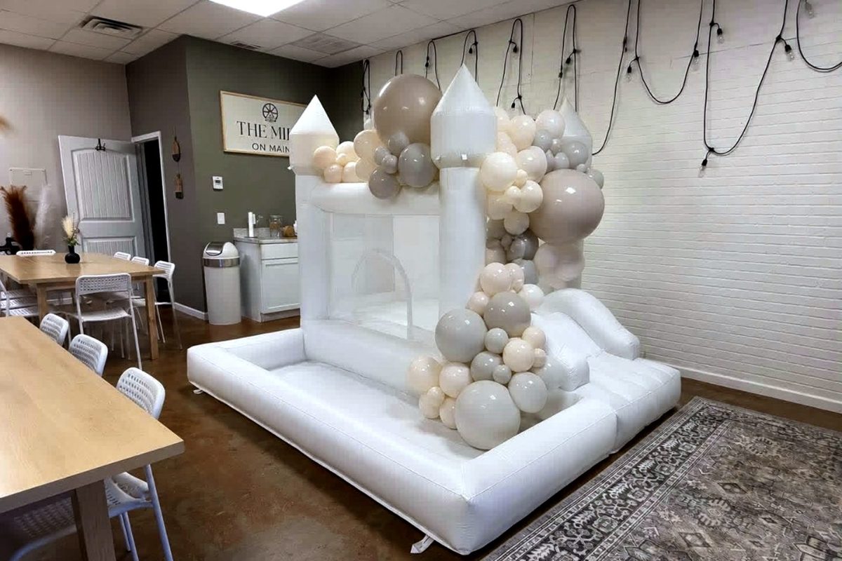 White bounce house with a cream and gold balloon garland set up for a celebration