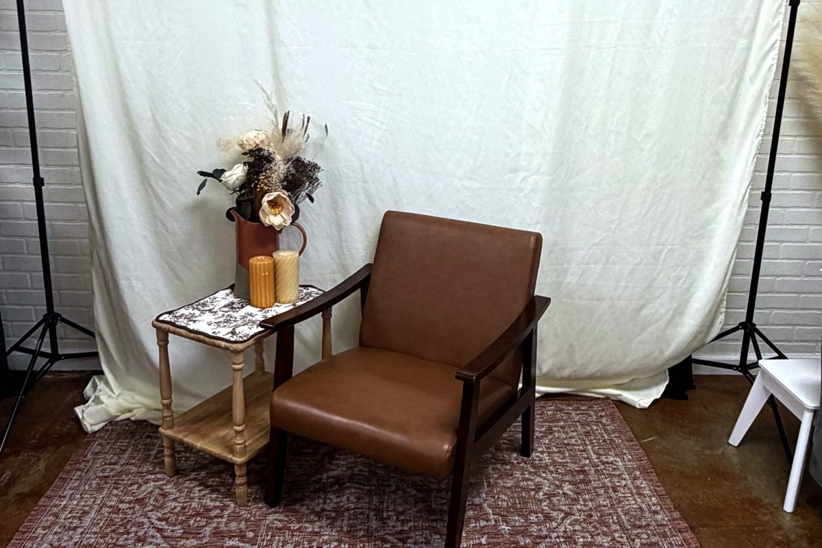 Photo corner with a leather armchair, side table with candles, and a cream backdrop on stands