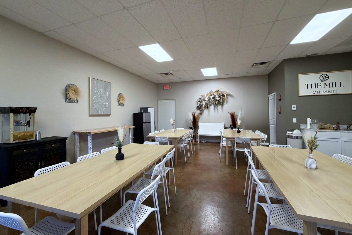 The full room with long wood tables, white chairs, dried-floral arrangements and The Mill on Main sign