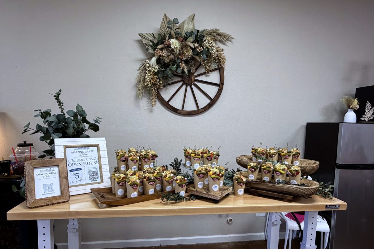 Table of party favors and framed signs beneath the wagon wheel with dried flowers