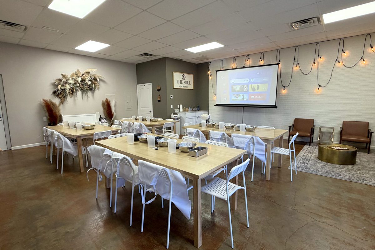Tables set for a workshop with white chairs, string lights, and a presentation on a pull-down screen