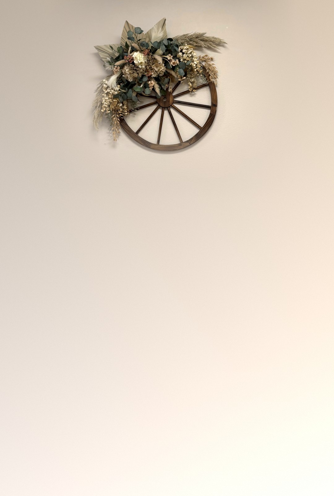Antique wagon wheel with a dried-flower arrangement on the cream wall at The Mill On Main